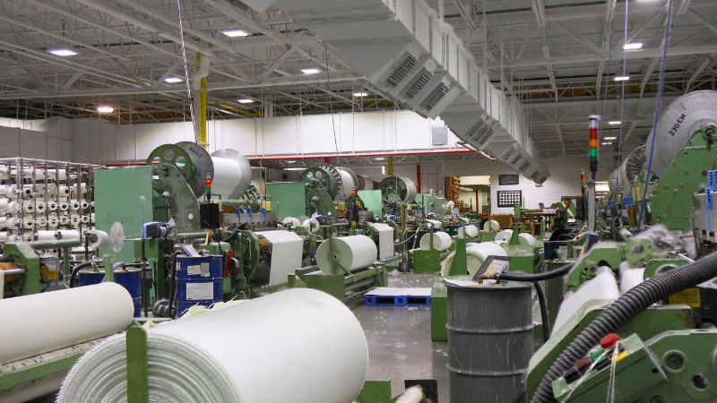 Interior of a textile factory with large machines, spools of white thread, and rolls of fabric.