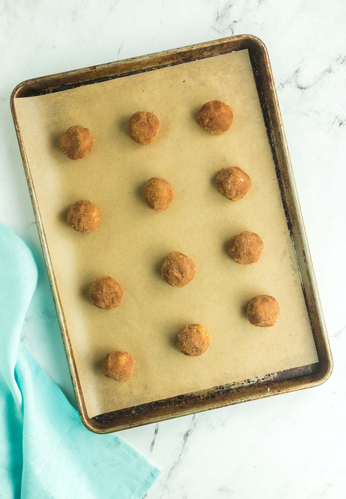 twelve brown butter pumpkin cookie dough balls on a parchment paper lined baking sheet