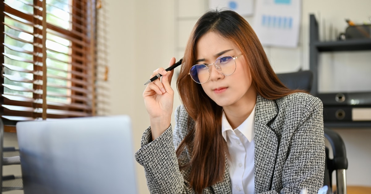 A focused woman in glasses analyzing documents on her laptop, strategizing high-income tax planning.