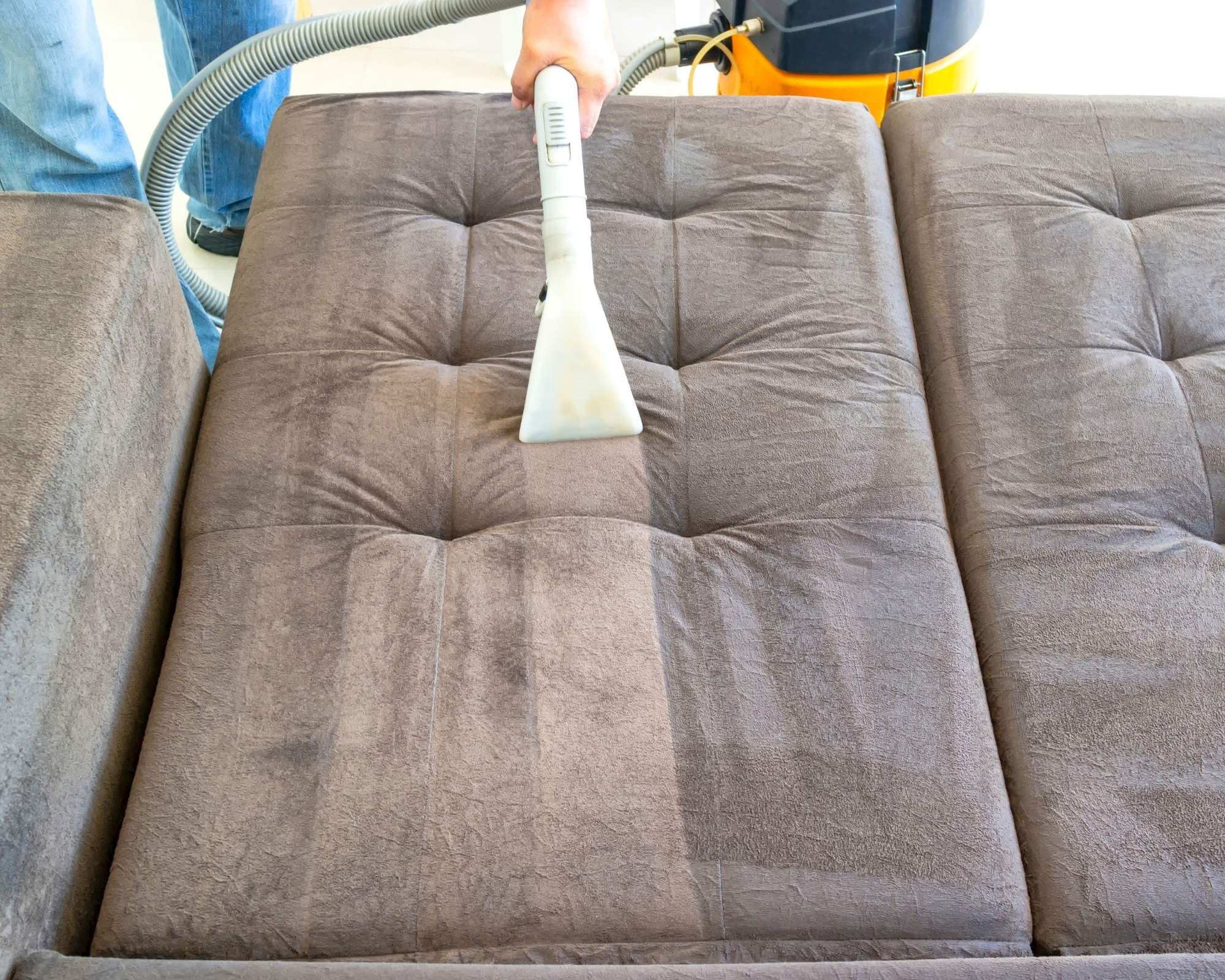 Professional deep cleaning a brown tufted sofa with an upholstery cleaner by Cleanology SG, showcasing expert sofa cleaning services to remove dirt and stains for a pristine finish in Singapore.