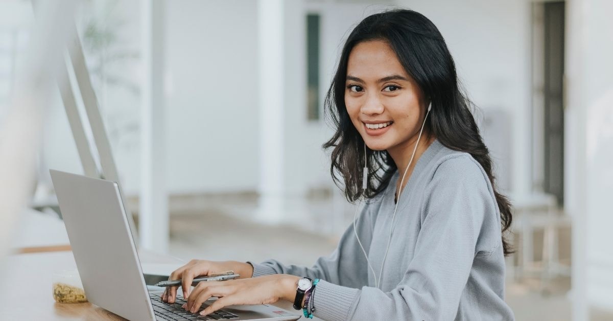 Smiling young woman working on her laptop, researching federal excise tax for OnlyFans creators.