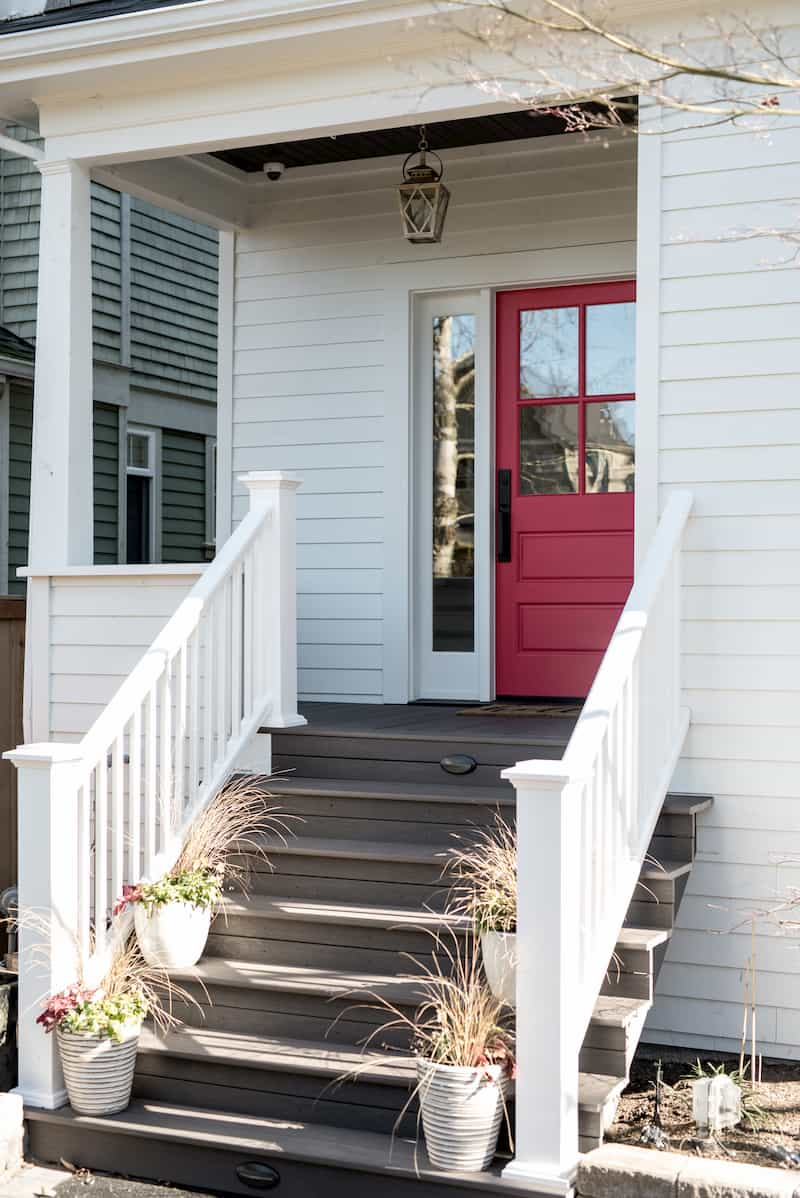Remodeled porch with a bright red door and new white porch railings.