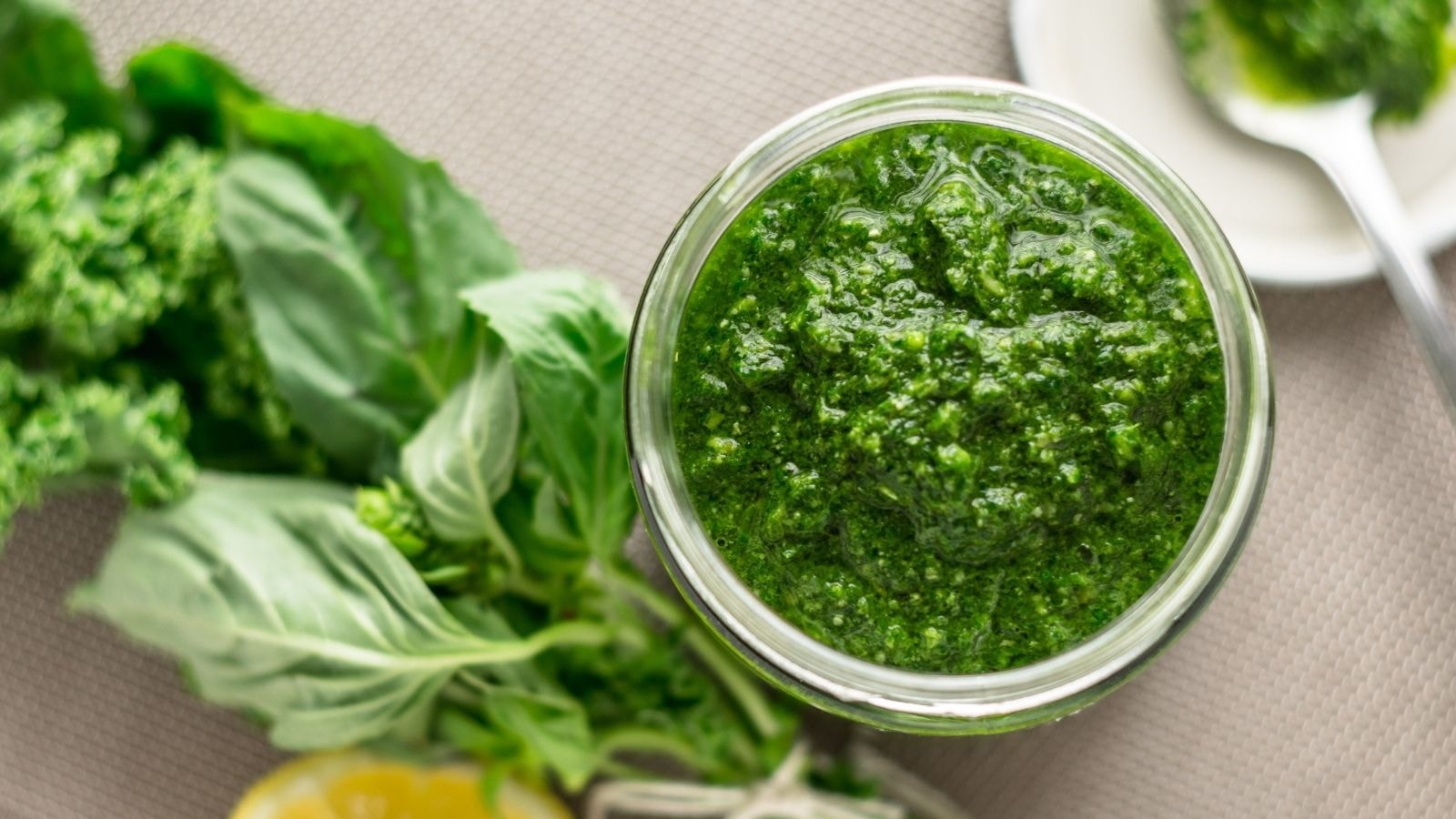 Jar of homemade basil pesto with fresh basil leaves in the background