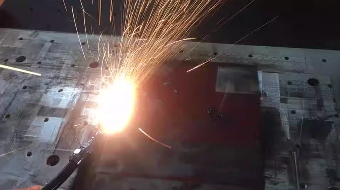 Laser cleaning machine creating sparks on a large, dirty metal surface.