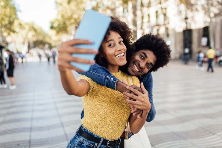 Cute couple smiling in the city sun and taking a selfie.