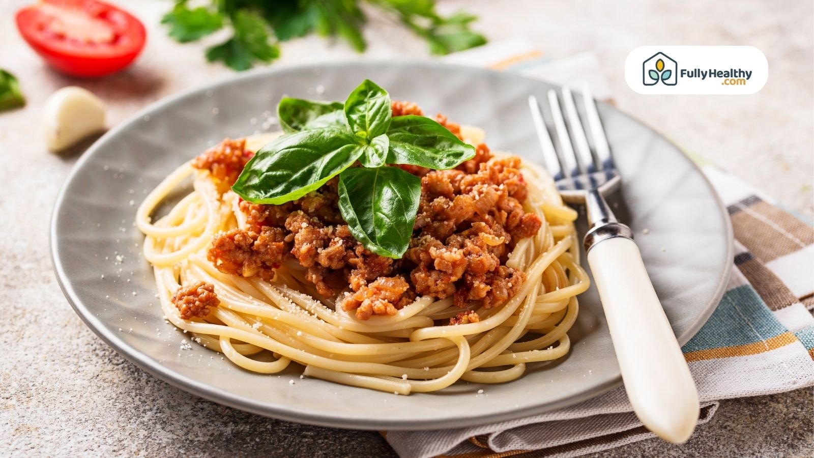Cooked spaghetti pasta topped with ground beef meat sauce and fresh basil on a grey plate