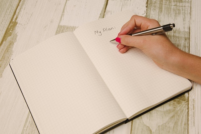 A person writing in a blank notebook with the title 'My Plan'.