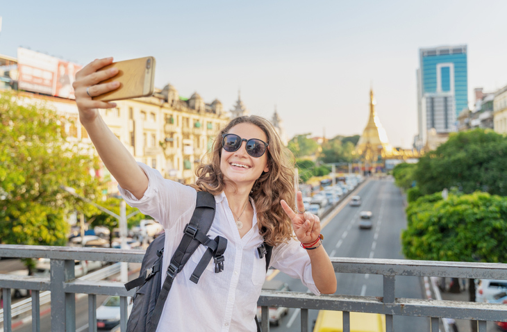 Cheerful woman snapping a selfie on an overpass with the view of traffic behind er.