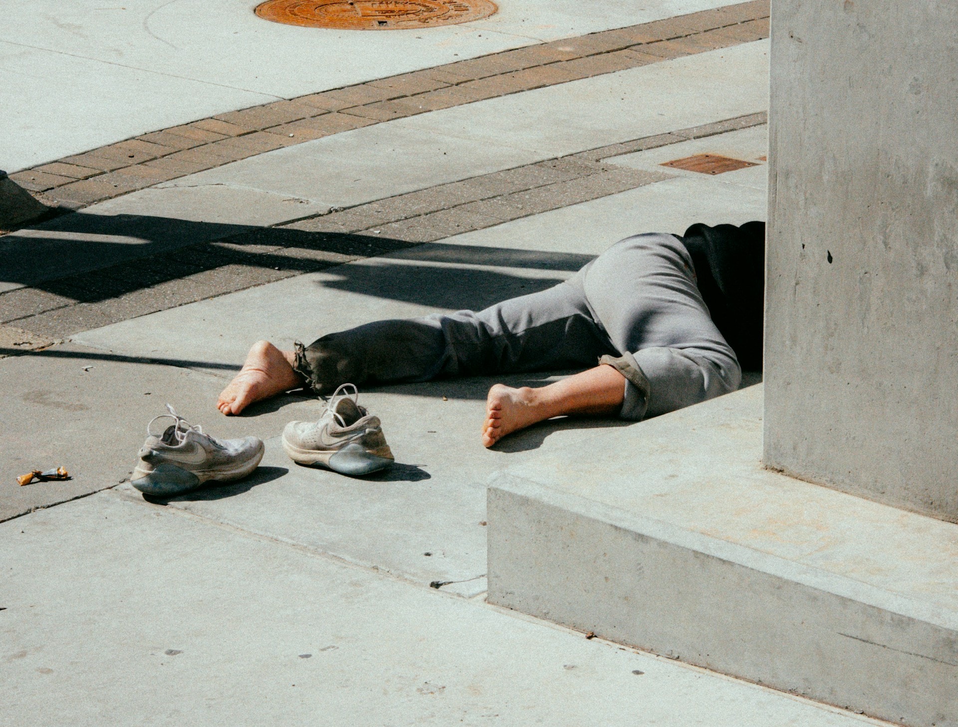 A man passed out drunk in a street in the day with no shoes on - https://unsplash.com/photos/person-in-gray-pants-and-gray-shoes-sitting-on-concrete-bench-S9C4euiw5y4