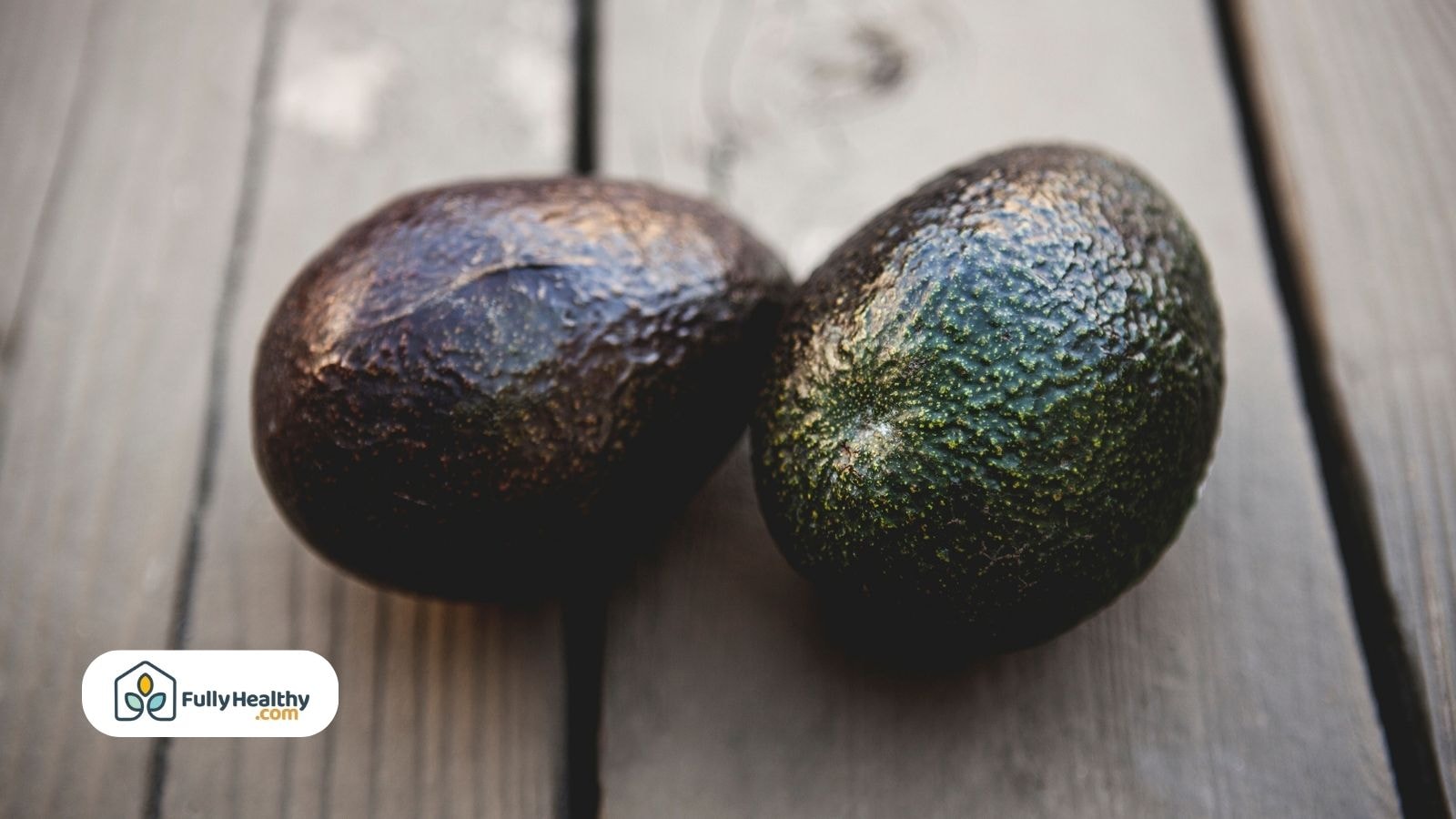 Two whole ripe avocados resting on wooden surface