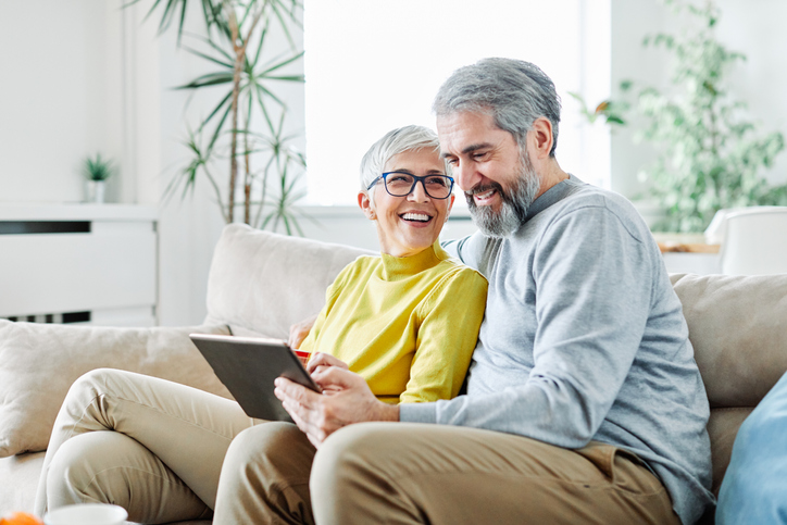 Cheerful man and woman sitting on a sofa smiling at a tablet.