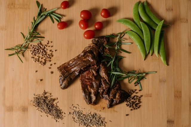Lamb dish surrounded by vegetables on a brown chopping board