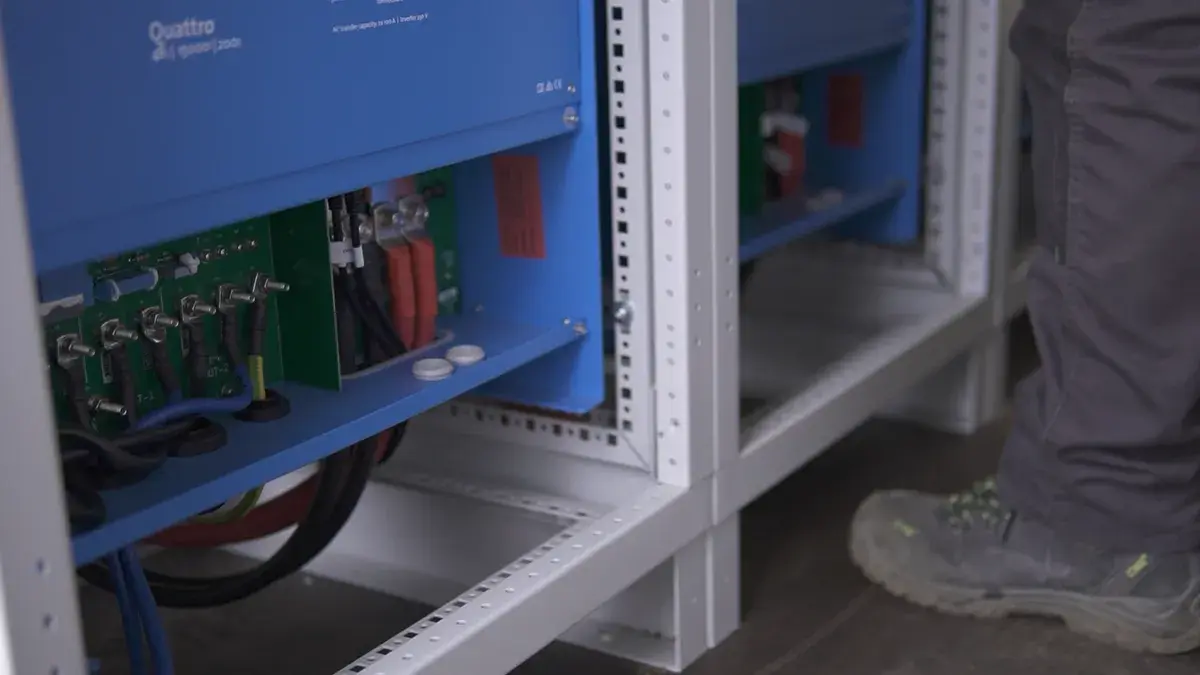 Na zdjęciu technik sprawdza szafę bateryjną oraz okablowanie w pomieszczeniu technicznym, co jest istotne dla systemów magazynowania energii, takich jak rozwiązania firmy Victron Energy. W tle widoczne są różne urządzenia związane z instalacjami fotowoltaicznymi i zasilaniem.