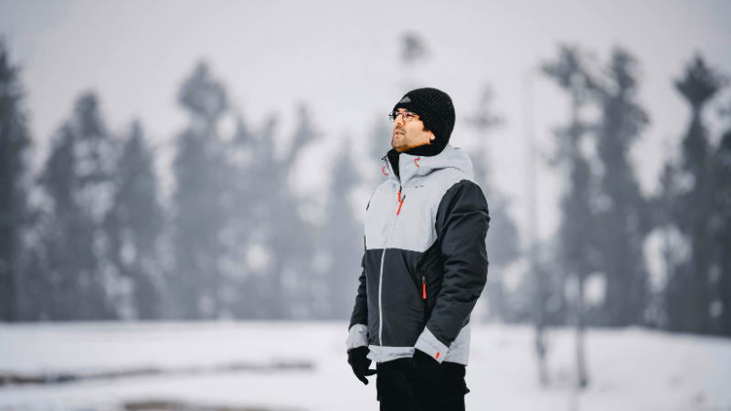A person in a black beanie and ski gorpcore jacket stands in a snowy landscape.