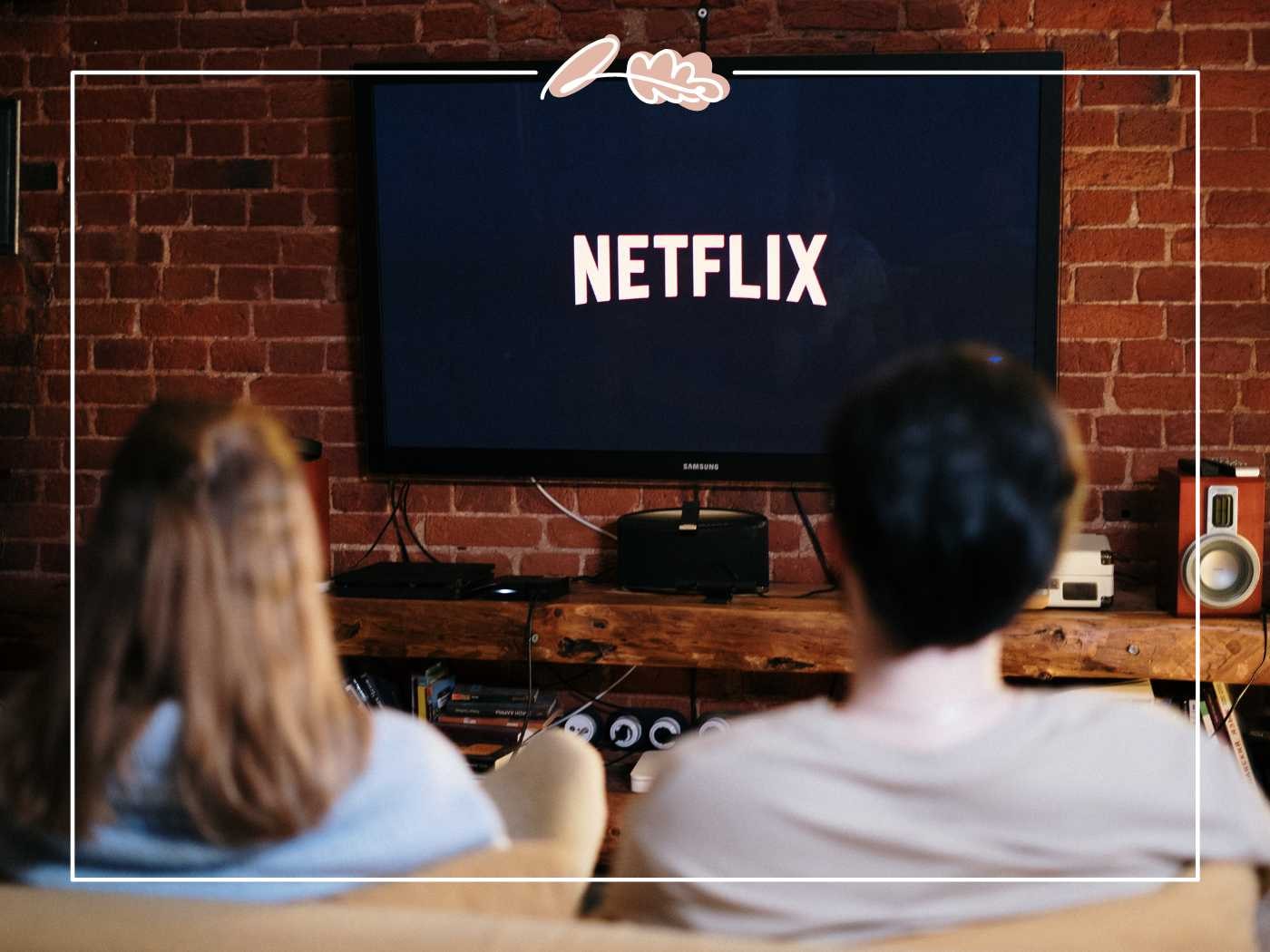 A couple sitting on a couch, watching Netflix on a wall-mounted TV in a brick-walled room - Fabulous Flowers and Gifts.