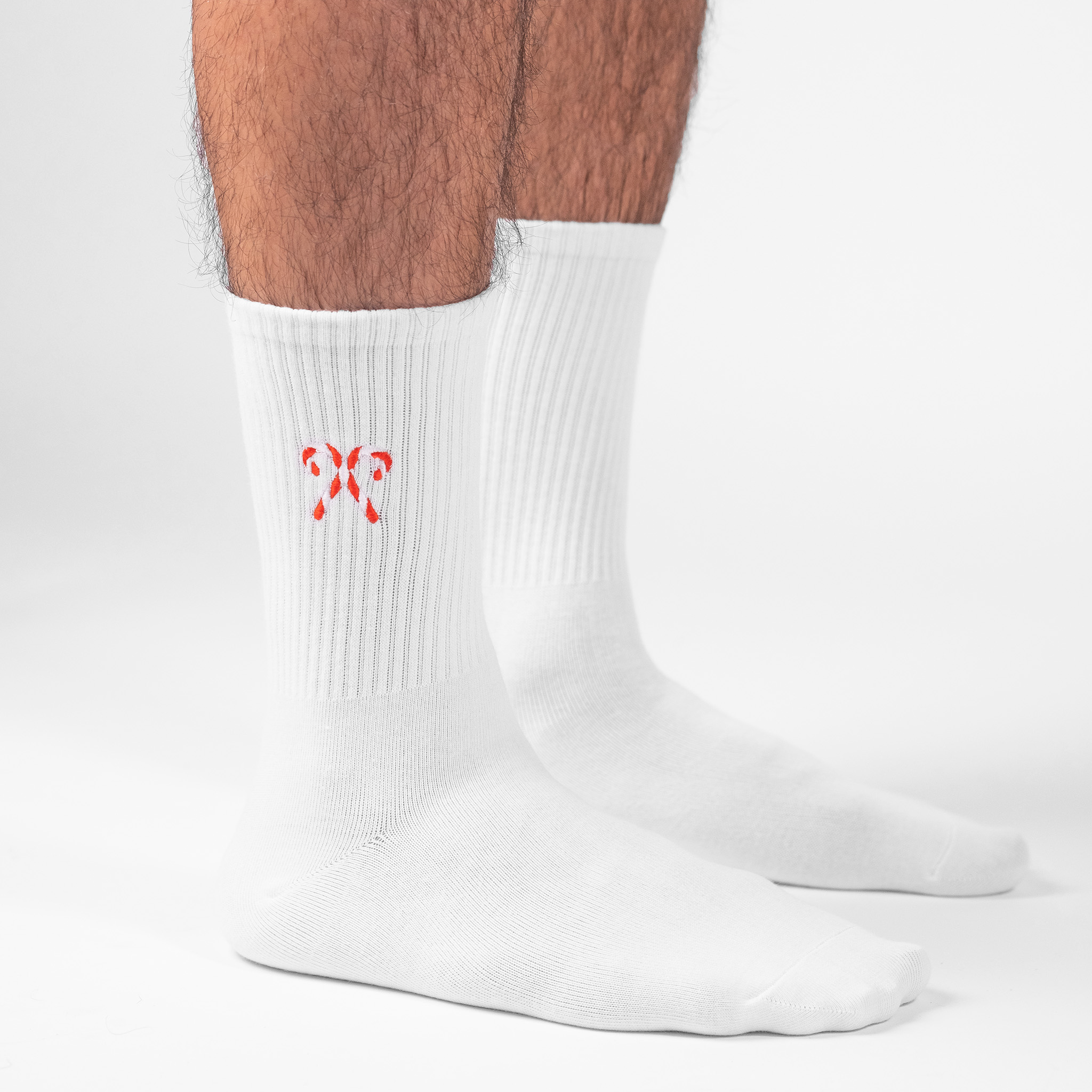 A male model wearing a pair of personalised white crew socks with the a candy cane embroidered onto each sock.