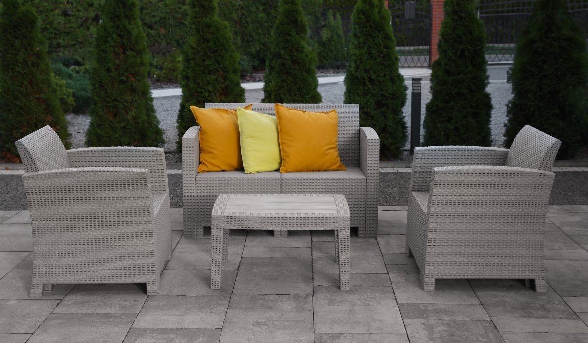 Rattan furniture - light gray patio furniture - two single chairs, double seat and small, low table - no upholstery just bright orange and yellow throw cushions
