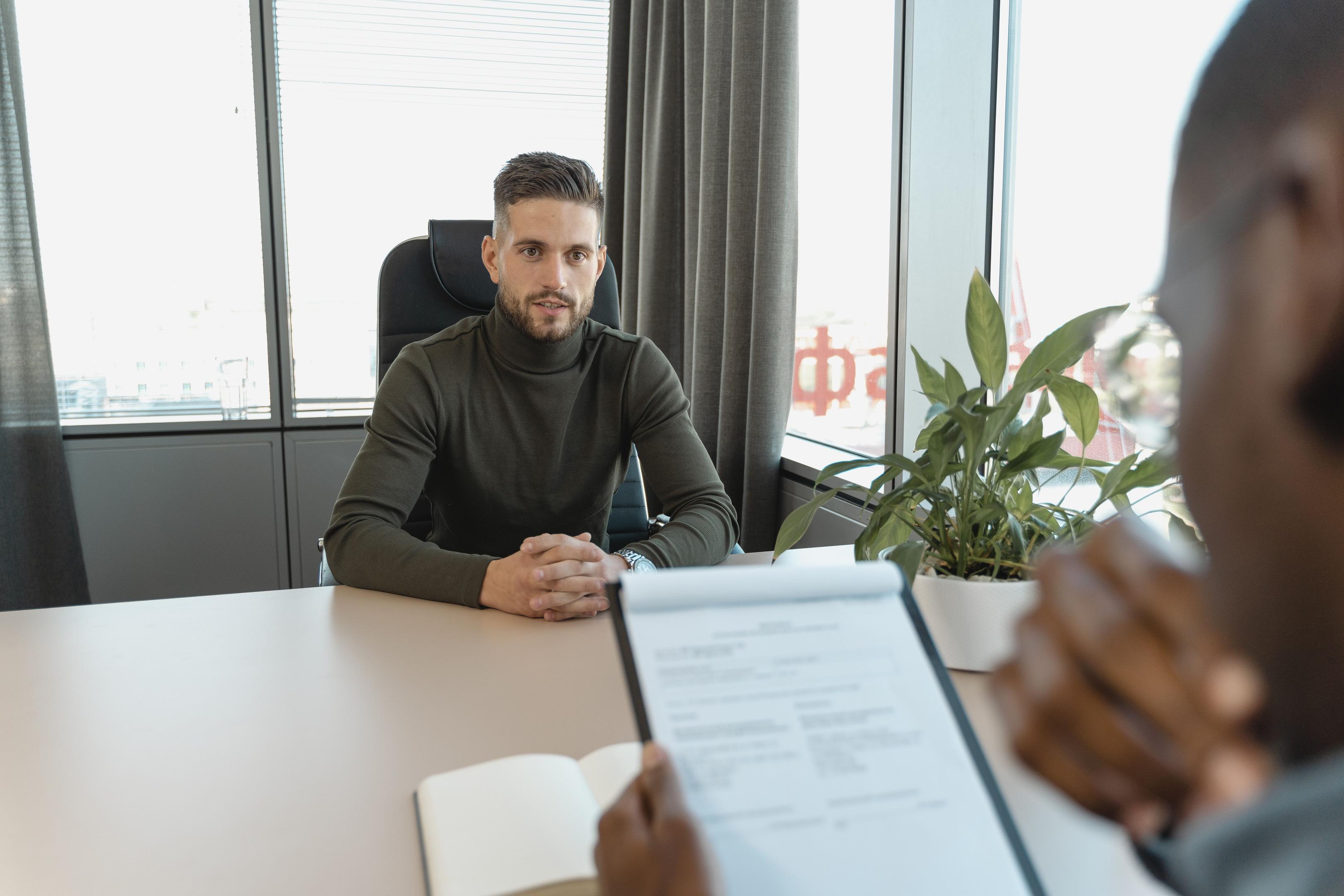Man with a clipboard sitting across a desk from another man.
