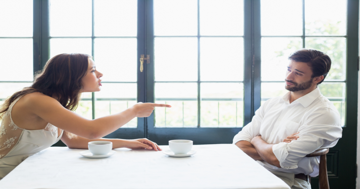 A photograph of a couple sitting across from each other at a table, with their faces tense and their hands resting on the table. The couple appears to be arguing or having a tense conversation, possibly related to a specific issue or conflict in their relationship. The image conveys the idea of a couple experiencing difficulties in their relationship that require the intervention of a certified Gottman Method Couples Therapist in New York City. The therapist can provide them with the tools and techniques needed to improve their communication, build emotional connection, and reduce conflict in their relationship.