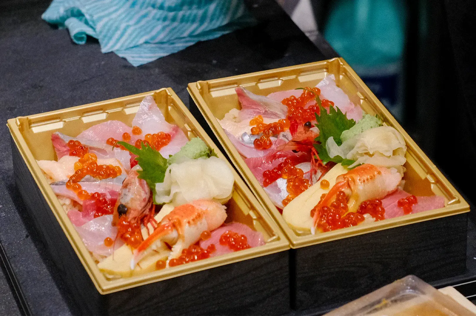Two Japanese seafood chirashi bento boxes topped with fresh sashimi slices, salmon ikra, sweet shrimp, crab claw, and pickled ginger.