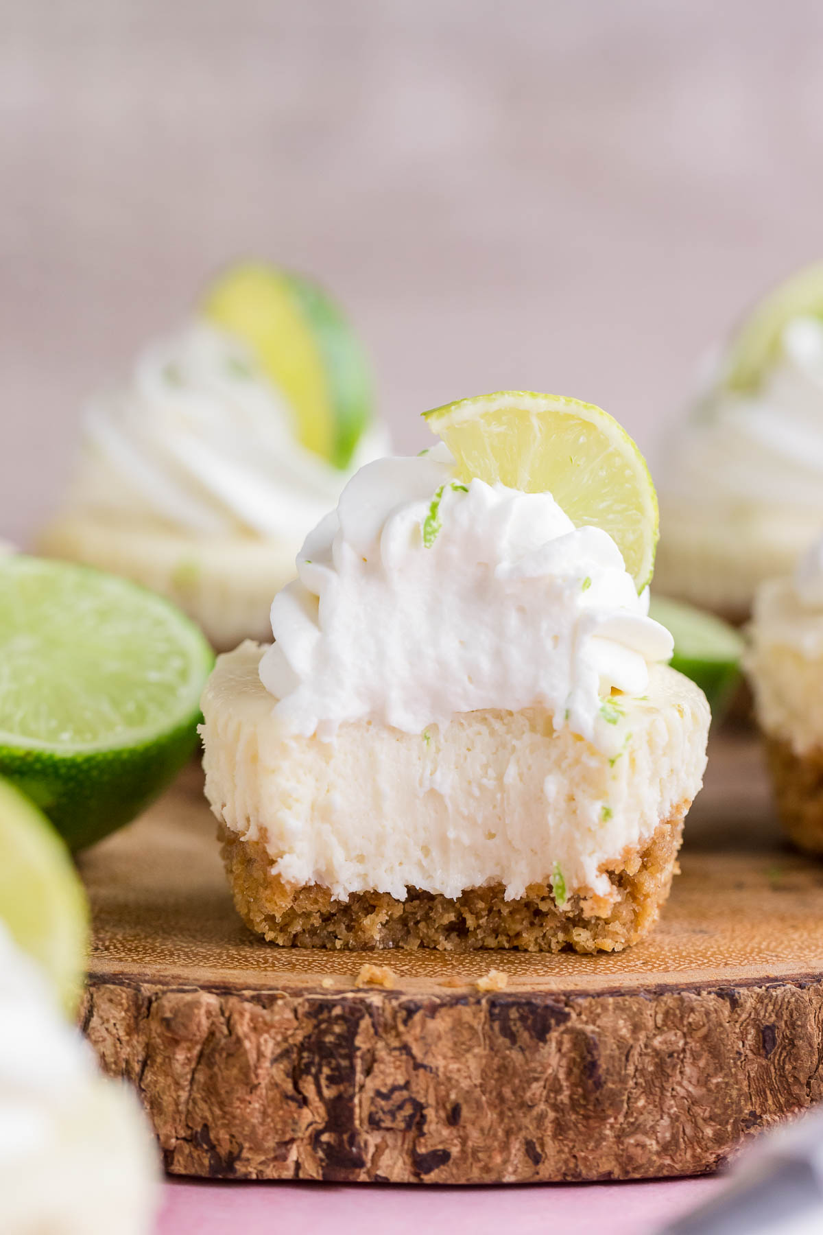 mini key lime cheesecake on a wooden cake stand with bite taken out of it