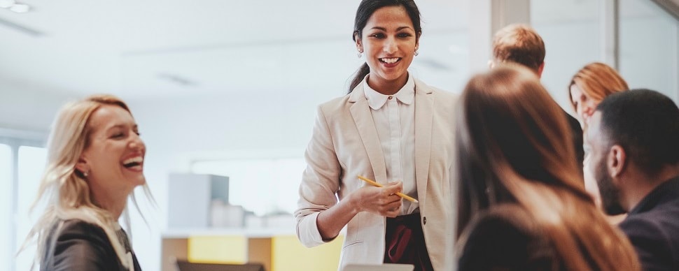 A group of white-collar employees smiling and laughing with each other in an office setting.