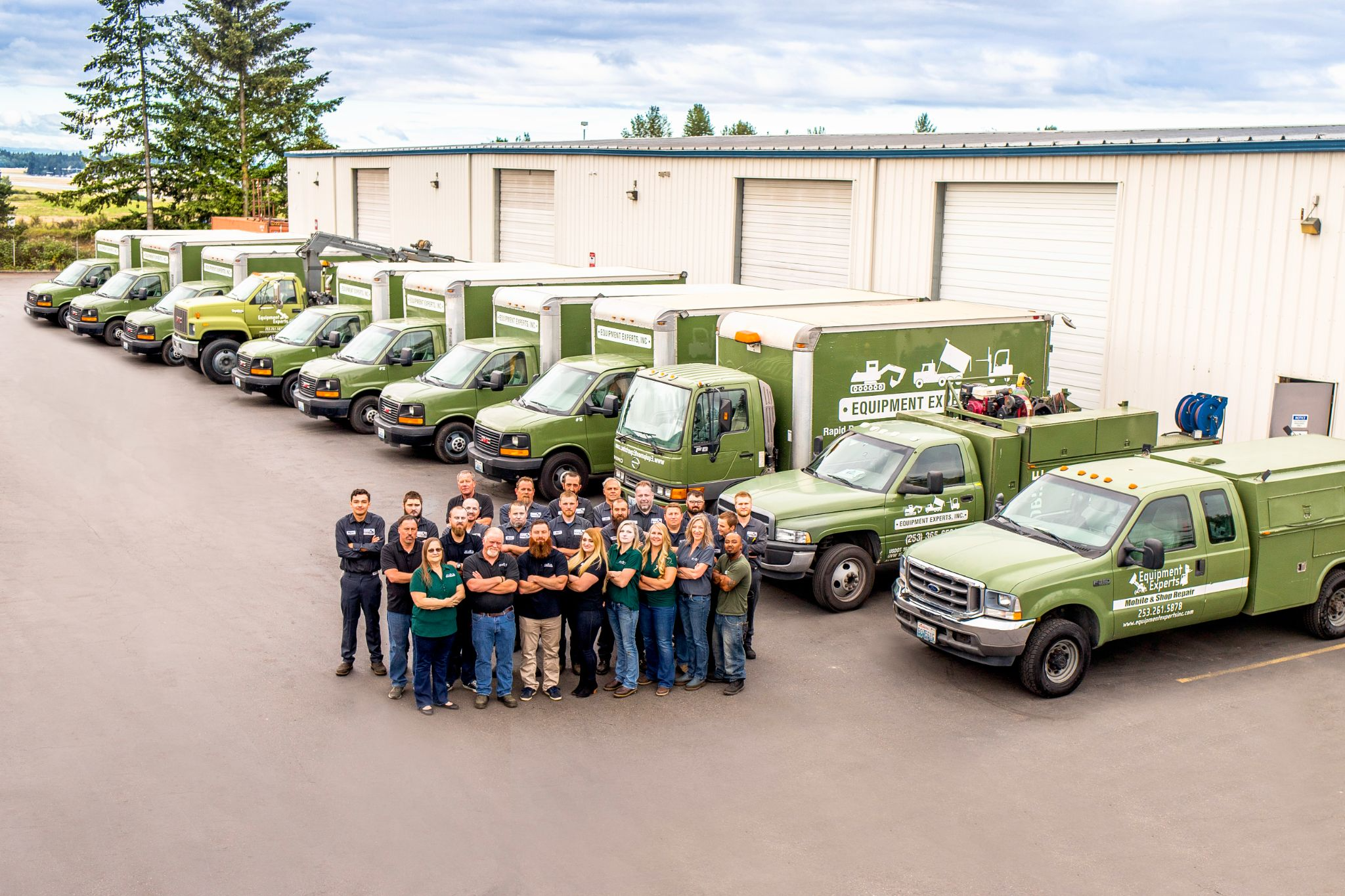 Equipment Experts, Inc. team with crossed arms in front of a fleet of trucks