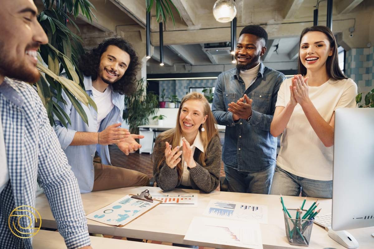 Smiling team members applauding a colleague, conveying support, encouragement, and shared success in the workplace.