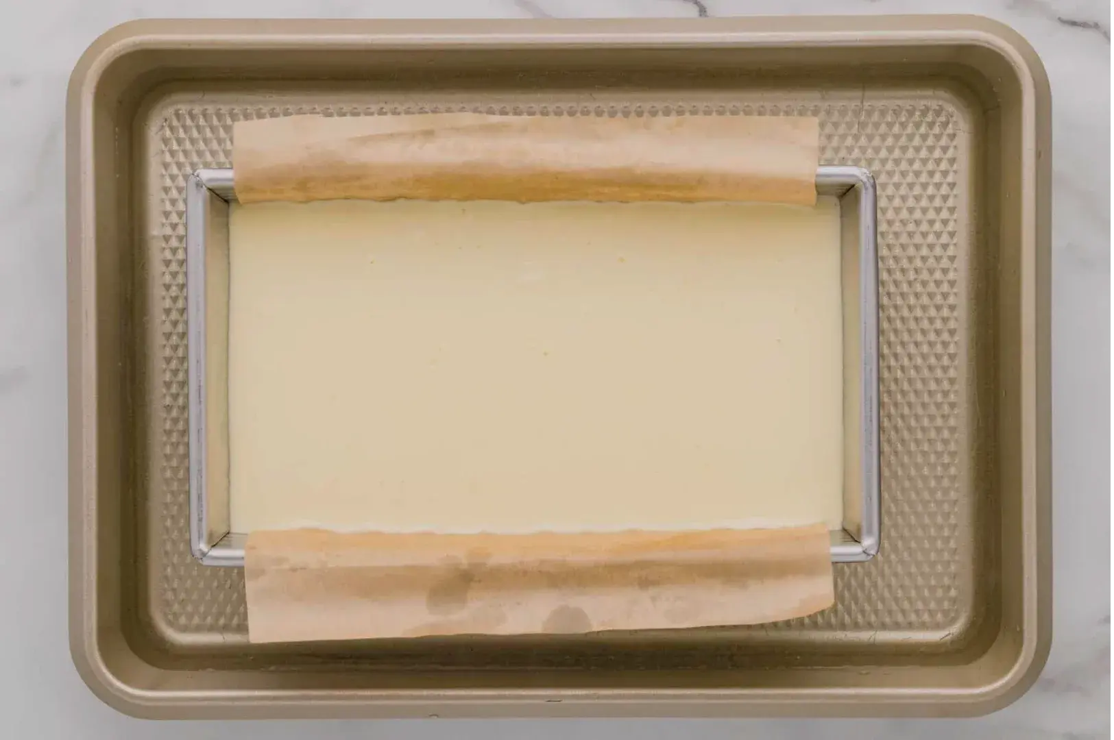A rectangular block of cream cheese or cheesecake batter in a baking tray lined with parchment paper.