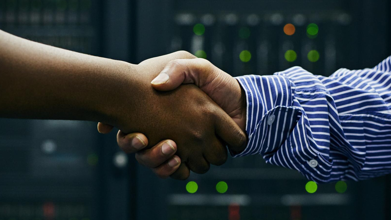 How Teams Chat and Slack Integration Enables Cross-Platform Messaging 5 Two hands shaking in front of server lights, representing how MSPs can build more partnerships with TeamMate's offering.