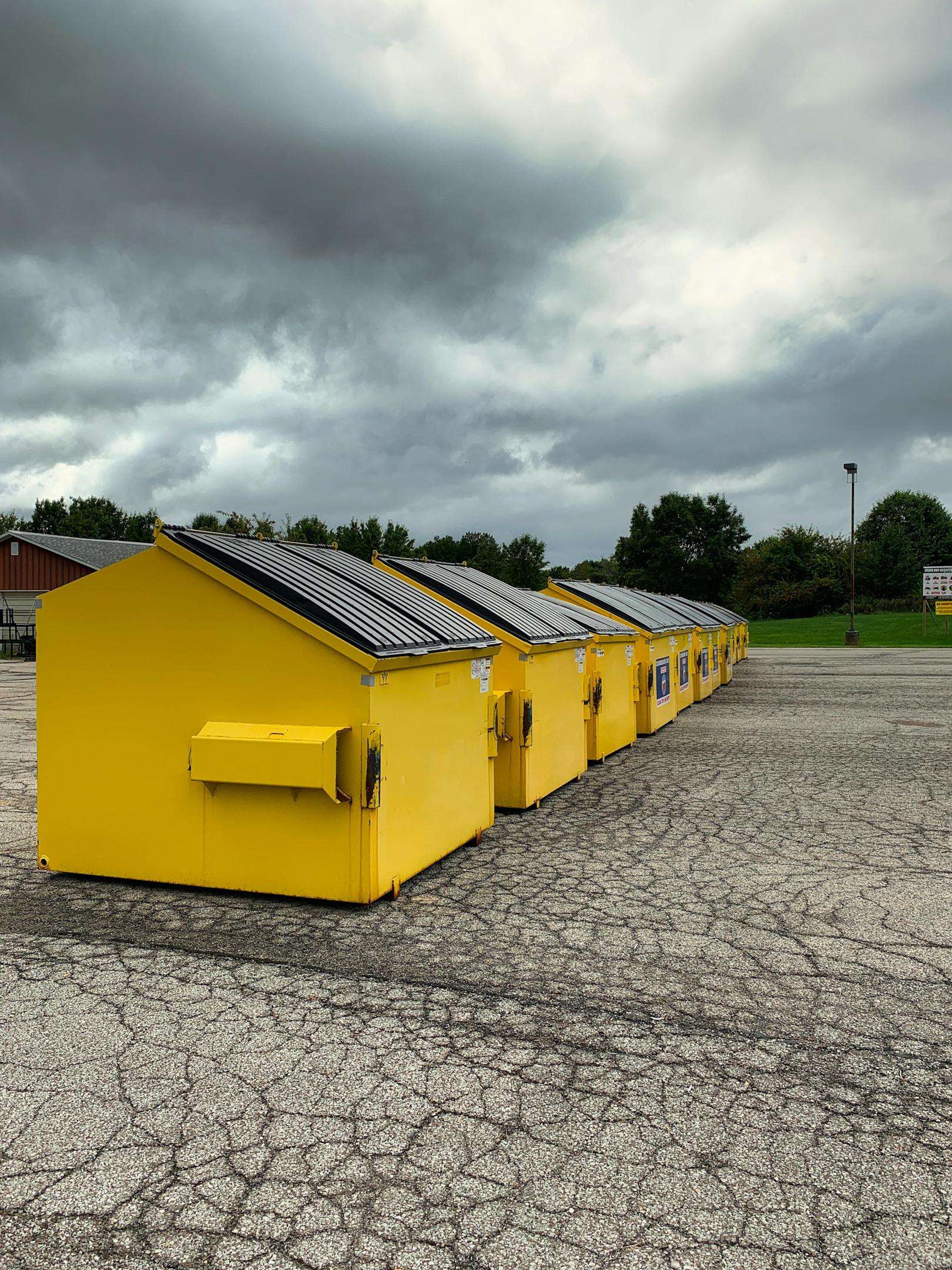 A row of large yellow dumpsters  with black lids