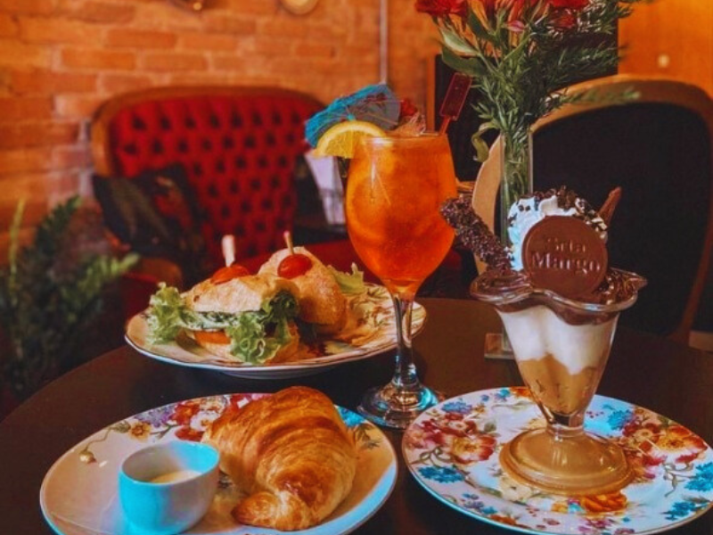 Pratos elaborados e drink sobre a mesa no Café Senhorita Margô em Porto Alegre. Imagem: Reprodução Instagram.
