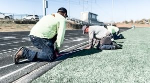 Crew installing a synthetic running track surface during track installation process.