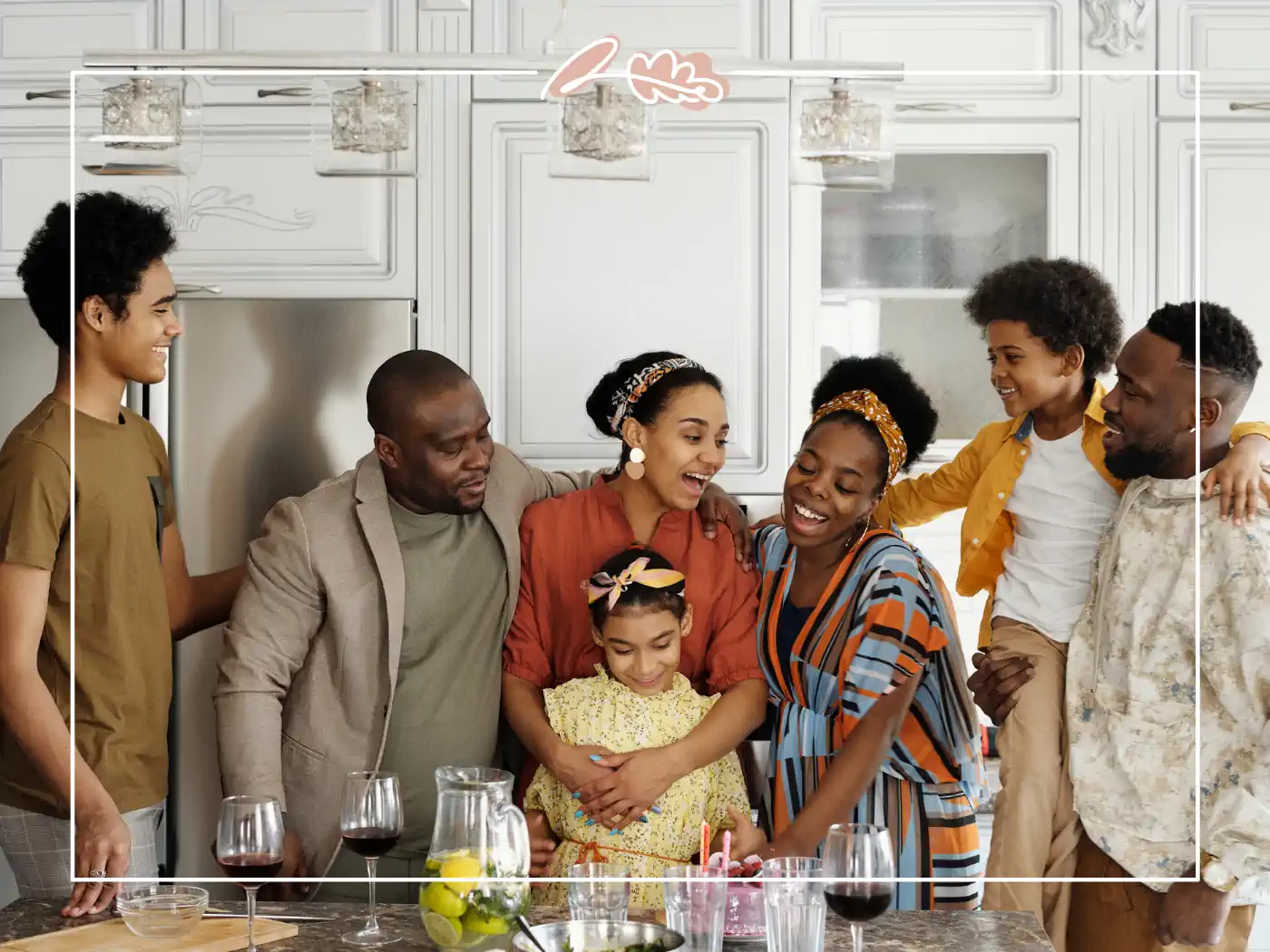 A family gathered in a kitchen, smiling and celebrating with a birthday cake. Fabulous Flowers and Gifts.