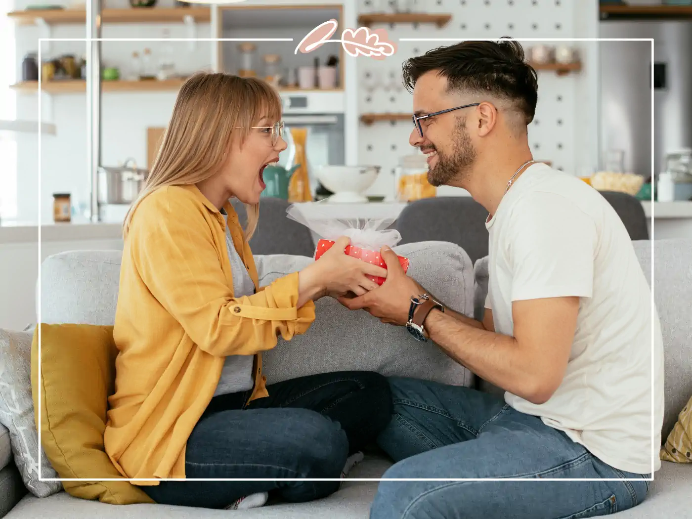 Man giving a red gift box to a woman on a couch, both smiling happily, Fabulous Flowers and Gifts