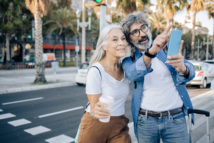 Mature couple walking on a city street and following directions on their phone.