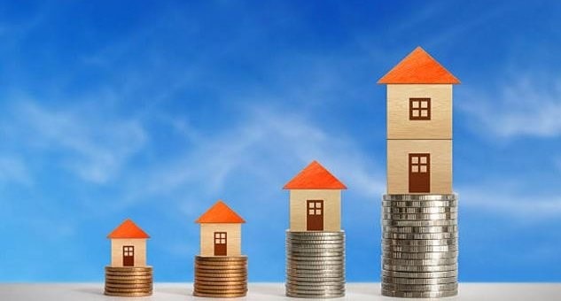 A picture of stacks of coins with block houses on them against a background with blue skies and white clouds.