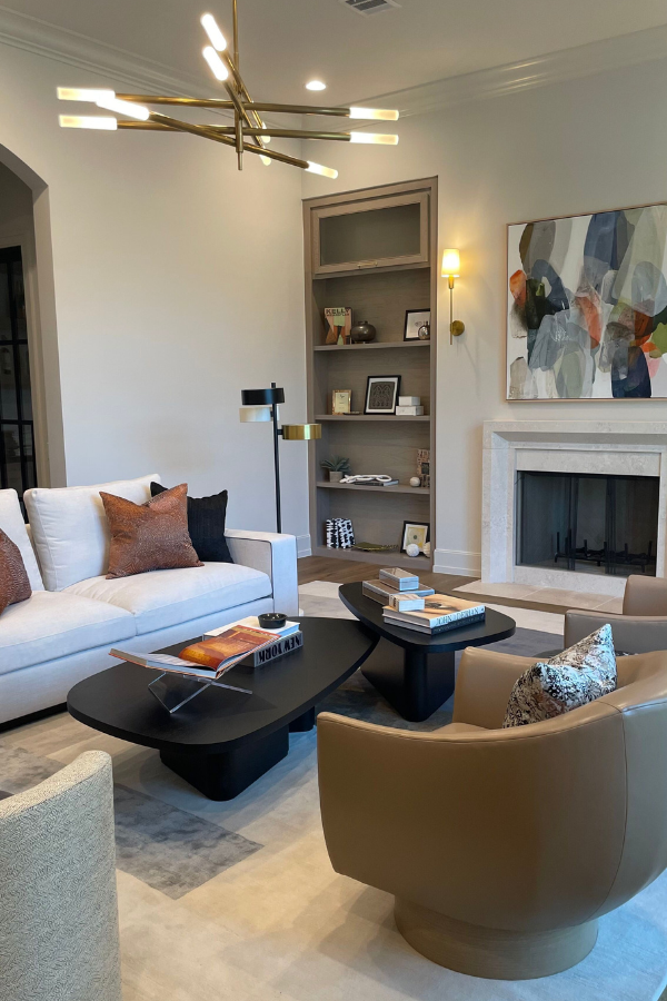 a living room vignette with built-ins, art, a sculptural pendant light, black coffee tables, club chairs, and. awhite sofa