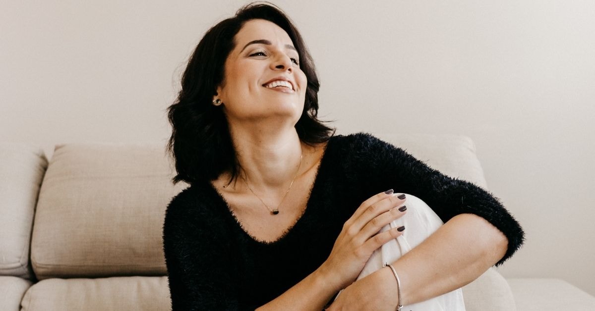 Brunette woman sitting on a couch, smiling with a relaxed expression – tax deductions list for self employed.