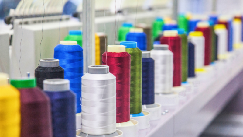 A row of polyester spools of colorful thread, including blue, red, green, and white, is lined up on a shelf, with some spools blurred in the foreground and background.