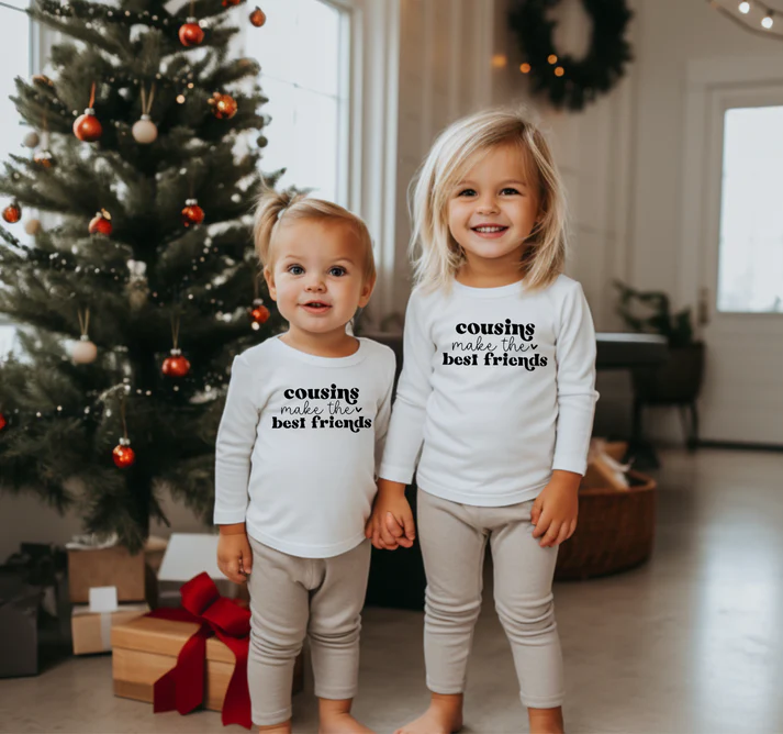 Two cousins in matching outfits in front of a Christmas tree laden with presents. Available for shipping
