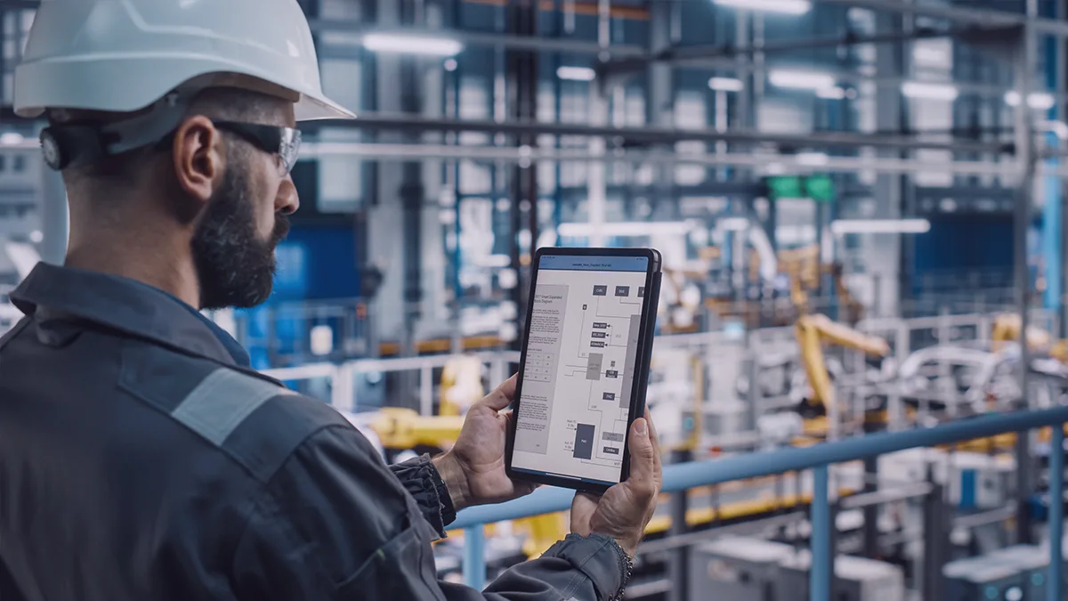 Engineer in a hard hat using a tablet to monitor production processes in an advanced manufacturing facility