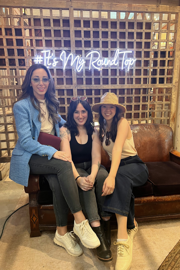 Three attendees seated on a leather sofa beneath a neon “It’s My Round Top” sign inside a vendor booth at the Round Top Antiques Festival.