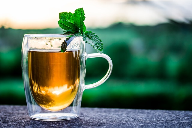 An image of a glass mug of peppermint tea with a sprig of peppermint on the rim.