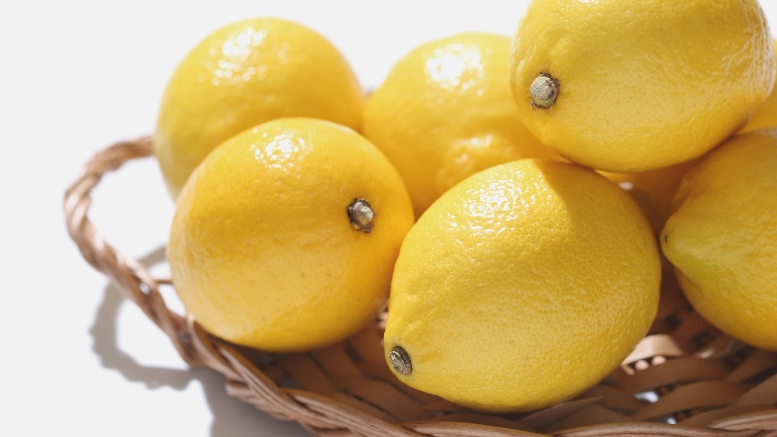 Fresh lemons in a woven basket on white background