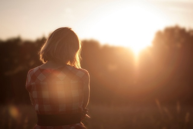 Woman staring into the sunset, wearing a pink dress, representing the idea of emotions associated with pathetic fallacy.