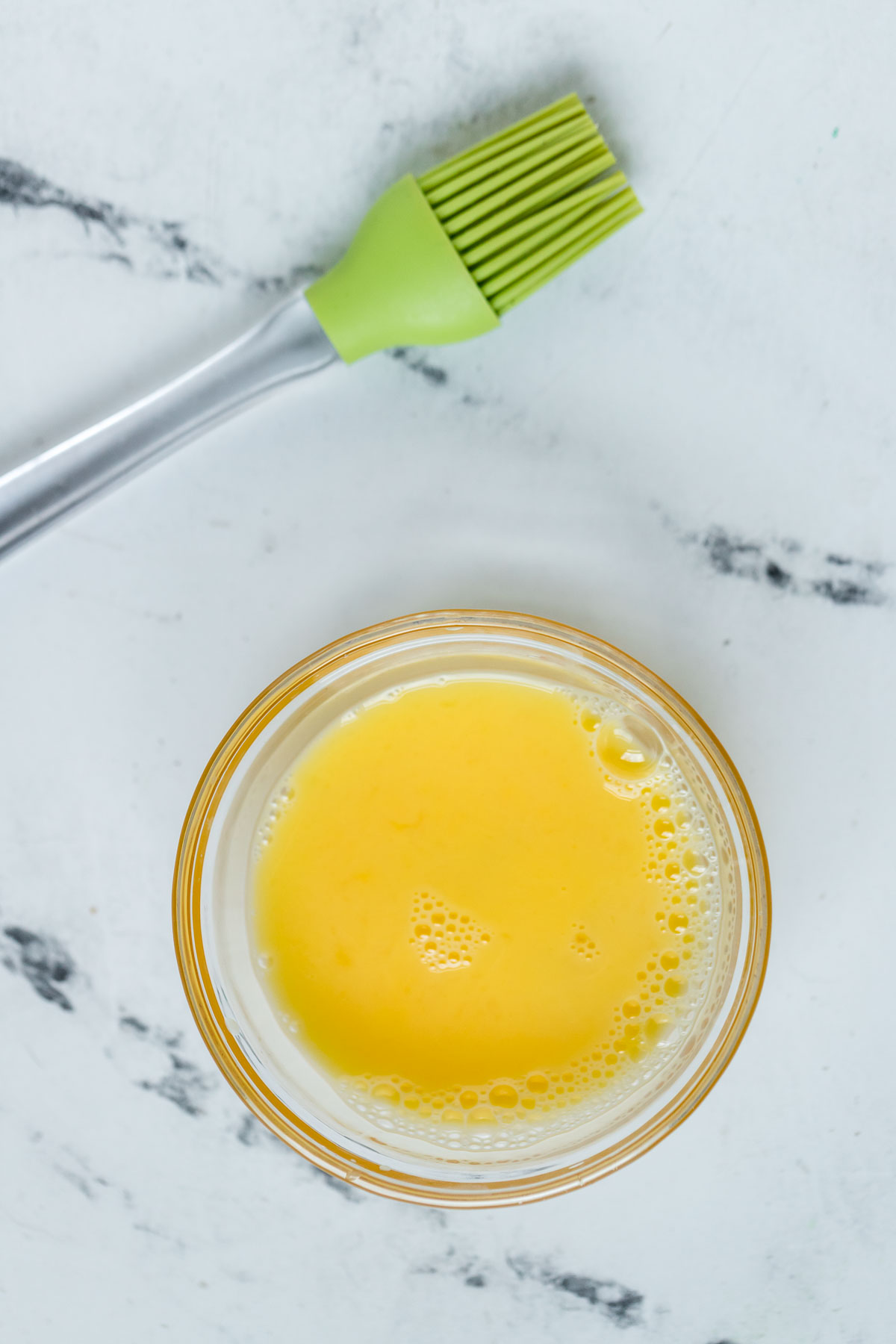 egg wash in a glass bowl with a green silicone pastry brush