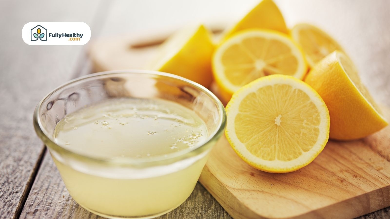 Fresh lemon juice in glass bowl with sliced lemons on cutting board