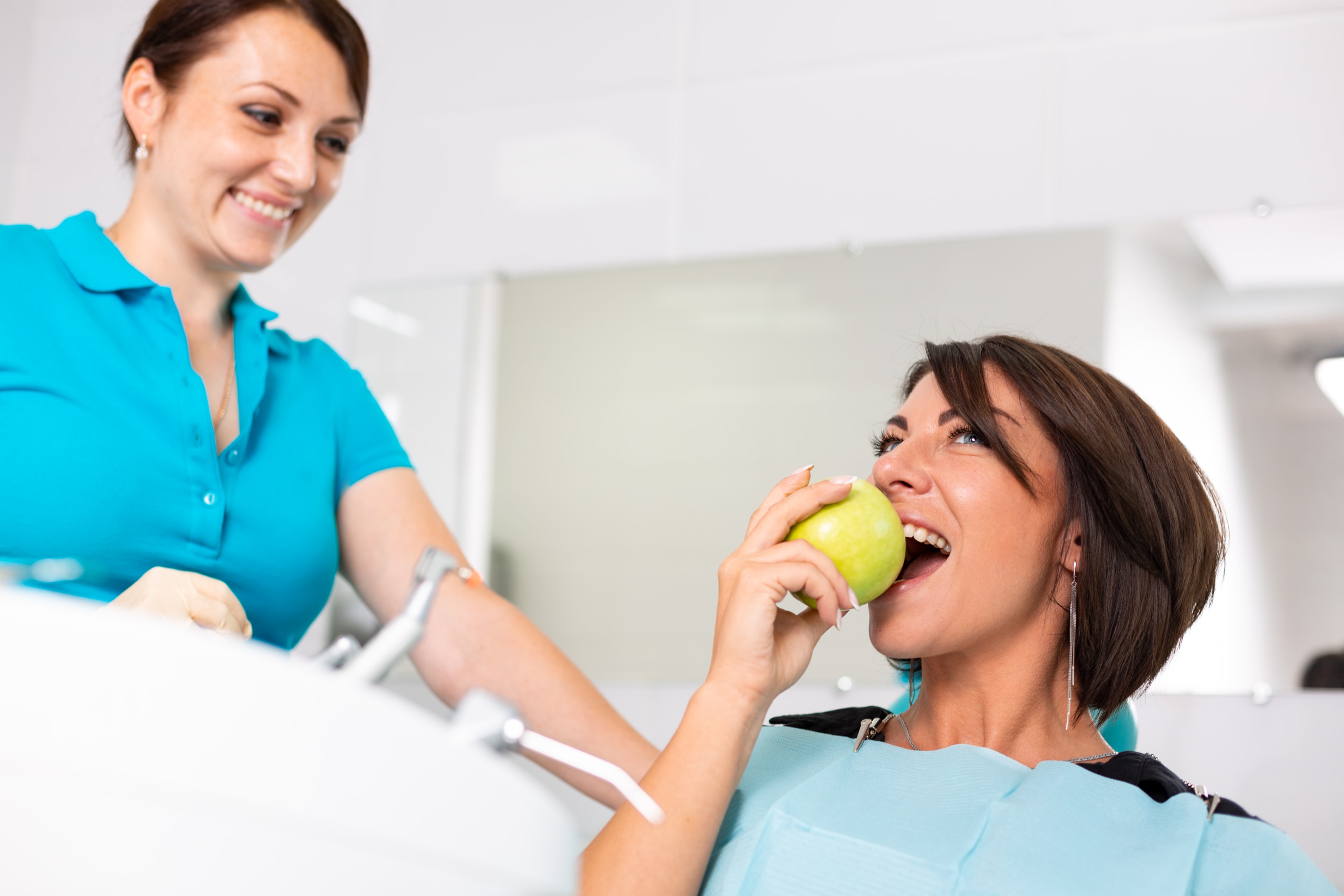 A happy young woman biting an apple knowing she has improved jaw function and appearance after surgery