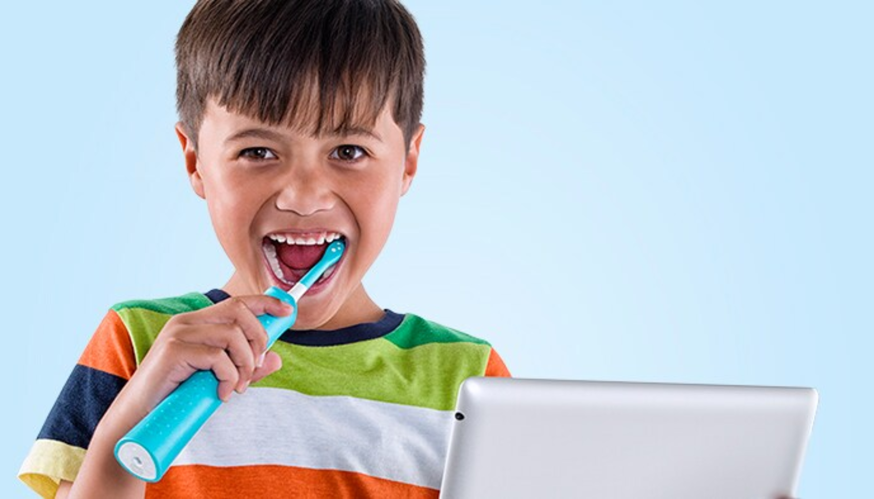 Elektrisk tannbørste for barn – Den smarte veien til bedre tannhelse 17 "Smilende gutt pusser tennene med elektrisk tannbørste mens han holder et nettbrett."